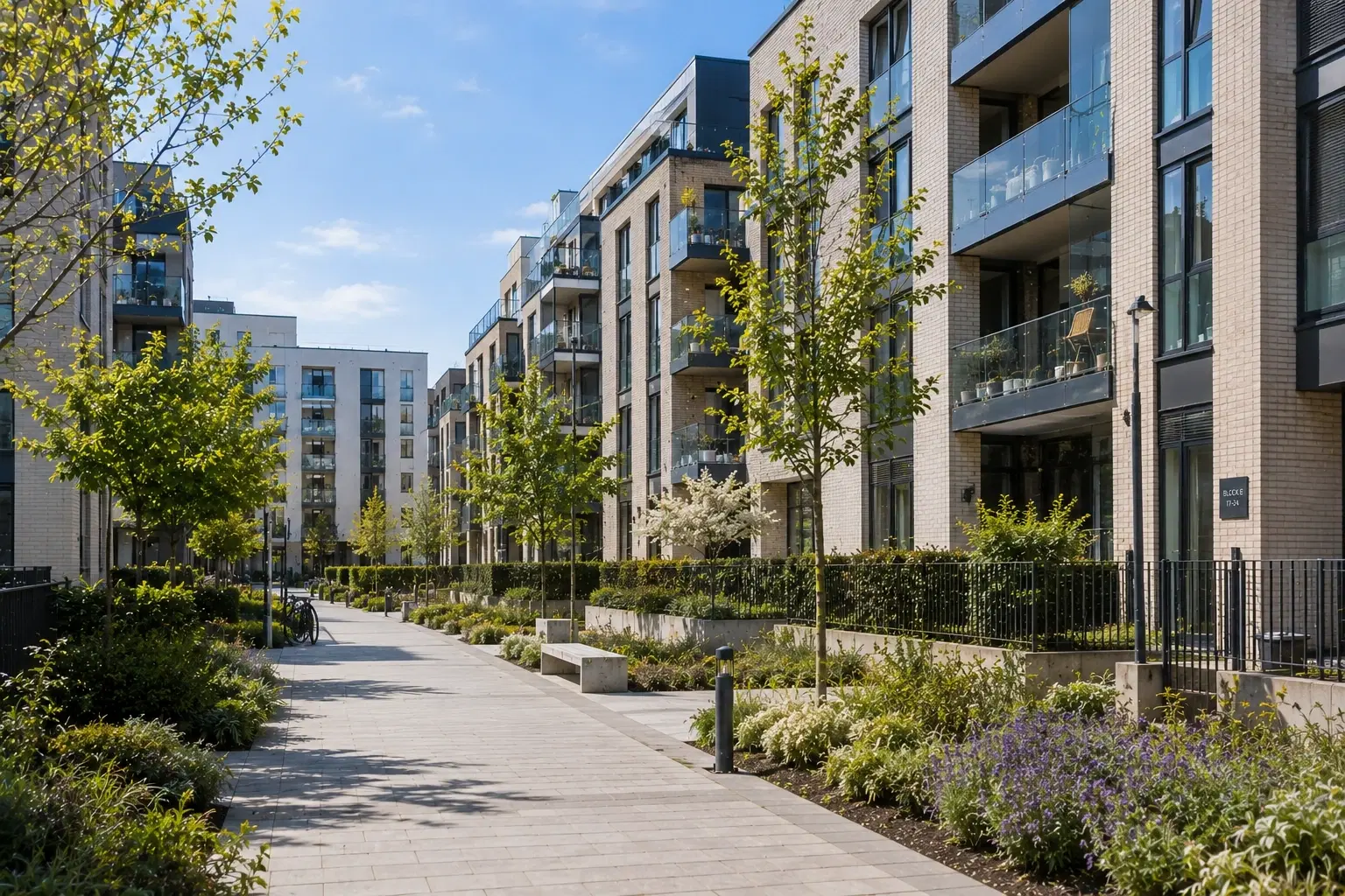 A landscaped pedestrian courtyard lined with trees and planting between modern apartment blocks at a residential development