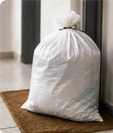 A tied collection bag waiting on a doormat inside an apartment door